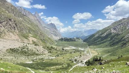 Fotobehang Olijf Alpine mountain range snow patches overcast sky dramatic clouds high altitude rocky peaks green slopes winding road valley panorama storm weather nature landscape view  © Марія Кучер