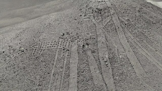Cinematic aerial view of ancient pre-Columbian geoglyphs carved into the dry desert surface of the Atacama in Chile.