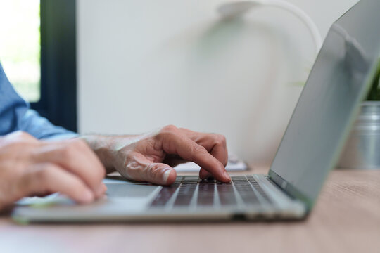 Close-up of a professional man typing on a laptop computer at a desk, working online with digital technology for business, communication, research, remote work and secure internet access.