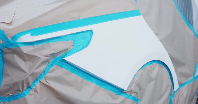 Car body panel masked and taped for paint preparation in automotive workshop, steady tracking pan across fender area.