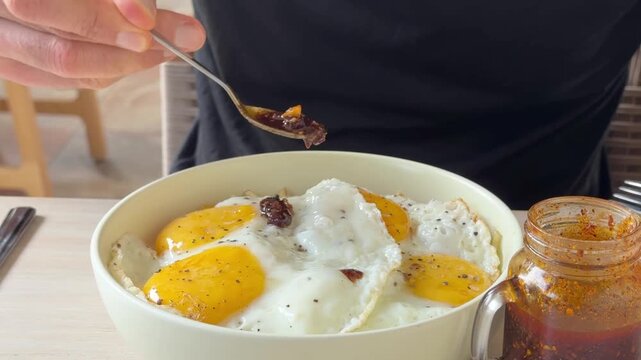 Spoon Drizzling Spicy Salsa Macha Hot Sauce Over Mexican Chilaquiles and Fried Eggs