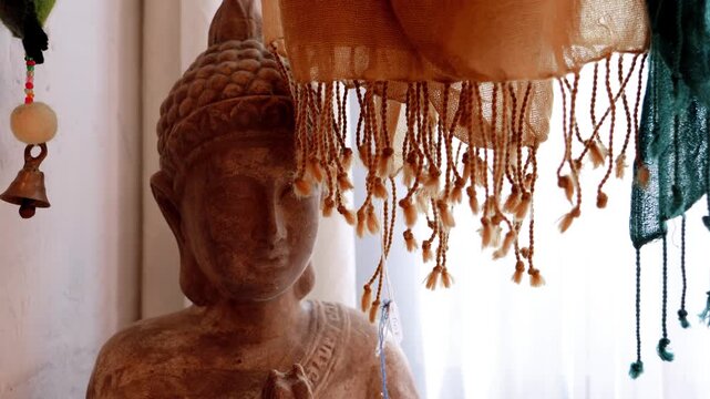 Serene Buddha statue with decorative scarf and prayer hands in soft light.