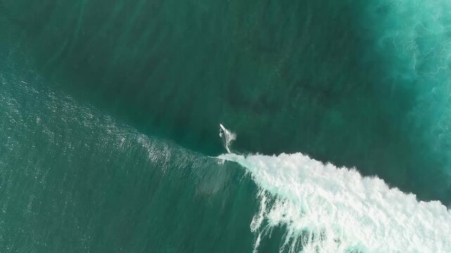 Aerial view of a surfer riding a turquoise wave in the ocean near South Kuta, Bali, Indonesia.