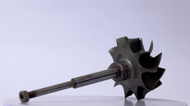Automotive turbocharger steel turbine wheel shaft rotor component on rotating display.