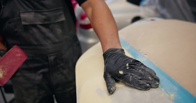 Tracking shot of auto body technician sanding and filling car door in workshop, garage fix concept.