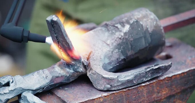 Close up heating and brazing of iron tool on rusted anvil at outdoor workshop.