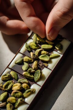 Hand arranging pistachio nuts on a white and dark chocolate bar for world chocolate day food blog banner and packaging