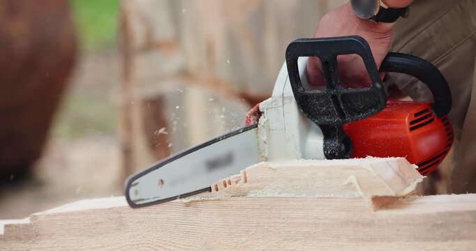 Slow motion closeup of person cutting wood plank with chainsaw on outdoor workbench during daytime. tracking handheld shot.