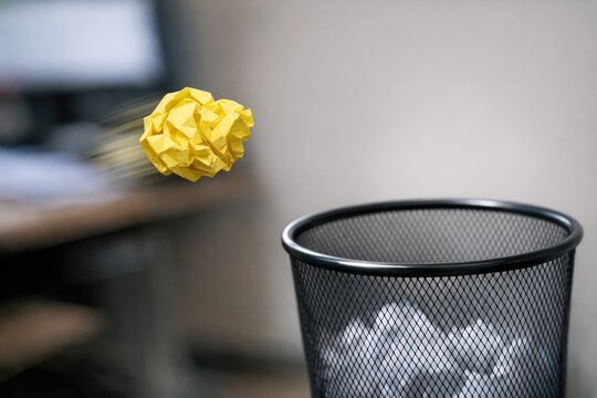 A discarded yellow paper ball floating on top of waste in a metal trash can