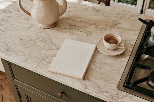 Handwritten grocery list and a cup of coffee on a marble countertop in a Parisian kitchen, showcasing a serene morning setting