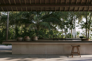 Fototapeta premium Outdoor kitchen in a Tropical Modernism villa in the Maldives featuring a slate limestone island and a teak bar stool under a timber-beamed roof