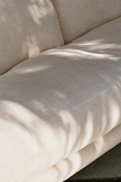 Closeup of cream linen cushion fabric on a Tropical Modernism daybed with soft natural creases and dappled afternoon light