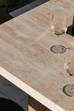 Closeup of pale travertine stone texture on a terrace bar top with wine glasses in warm evening light at a Tropical Modernism villa