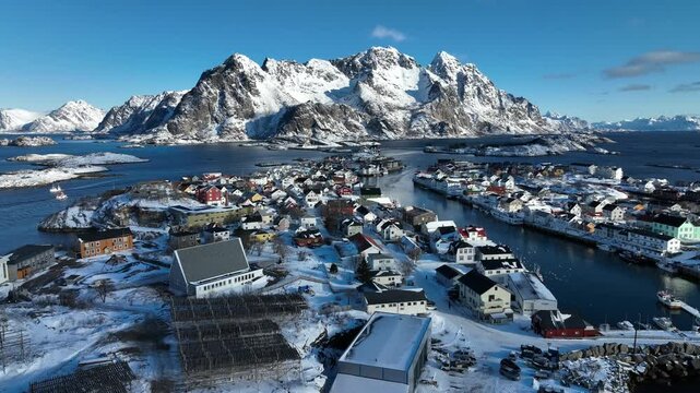 Aerial view of Henningsvaer village with colorful houses, snow-covered mountains, and icy waters in Henningsvaer, Nordland, Norway.