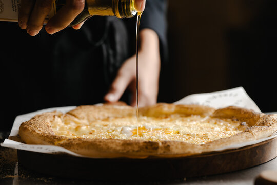 Pouring Olive Oil over Freshly Baked Pizza Crust in Restaurant Kitchen