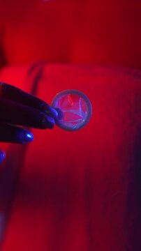 An unidentified woman wrapped in a towel under neon lights holds an unopened latex contraceptive condom to protect against sexually transmitted diseases and prevent accidental pregnancy.