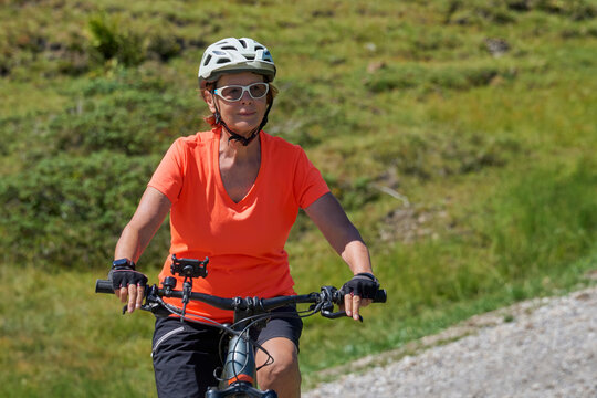 Attractive senior woman riding an electric bicycle on a mountain biking tour through sunny alpine meadows and scenic mountain landscapes above Balderschwang, Allg&auml;u Alps, Bavaria, Germany.