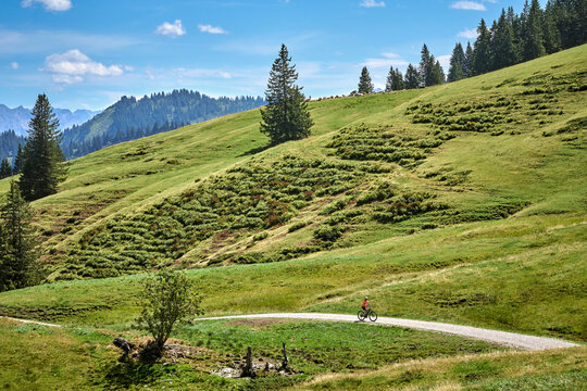 Attractive senior woman riding an electric bicycle on a mountain biking tour through sunny alpine meadows and scenic mountain landscapes above Balderschwang, Allg&auml;u Alps, Bavaria, Germany.