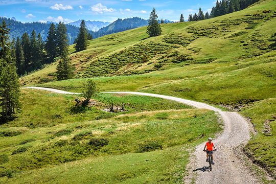 Attractive senior woman riding an electric bicycle on a mountain biking tour through sunny alpine meadows and scenic mountain landscapes above Balderschwang, Allg&auml;u Alps, Bavaria, Germany.