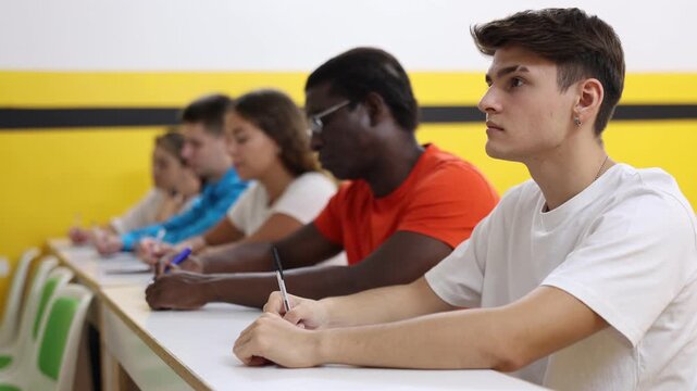 Teenage boy studying in taxi driving school, sitting at his desk with group of people.