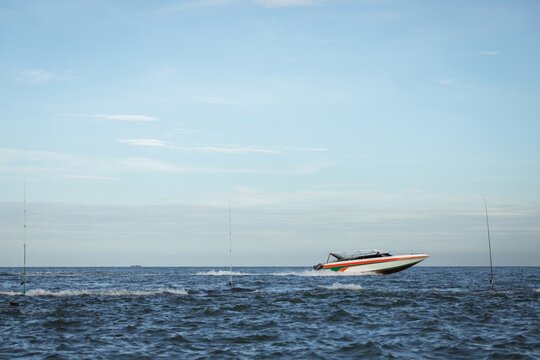 White and red speedboat cruises across calm blue sea near three vertical fishing rods