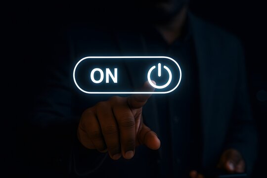 Dark-skinned hand reaches out in the darkness to press a glowing white "on" toggle switch button, indicating activation or a new beginning.
