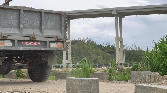 Self-made three-wheeled cargo vehicle carrying goods on a small bridge across a river with a highway overpass in Vietnam