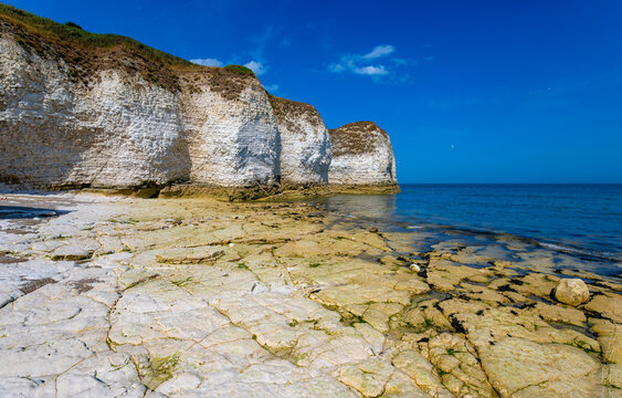 Impressive white chalk cliffs and exposed rock platform at Flamborough Head on the Yorkshire coast of England. The geological formations meet the blue waters of the North Sea.