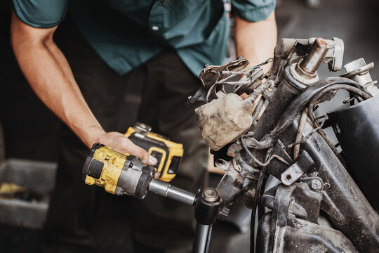 Mechanic using cordless impact wrench to disassemble motorcycle front fork and frame in garage