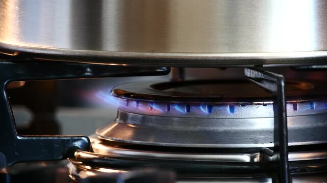 Macro shot of a blue gas flame on a kitchen stove burner heating a stainless steel pan.