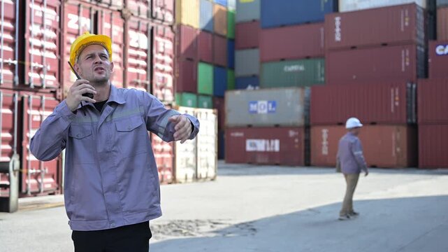 One female logistics worker uses a two way radio and hand signals to direct cargo operations at a shipping container yard. Concept of logistics, freight transport, communication, and supply chain.