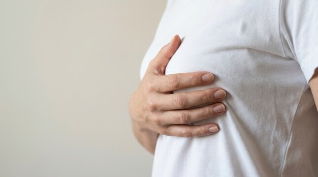 Woman's hand gently touching her chest area wearing a white t shirt cancer patient
