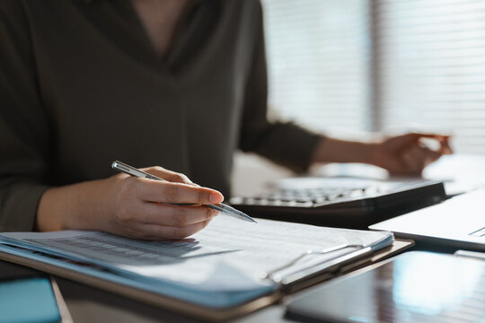 An accountant writes on a budget report while checking a calculator, using financial analysis, planning, expense, revenue and variance review to turn budget figures into a practical forecast.