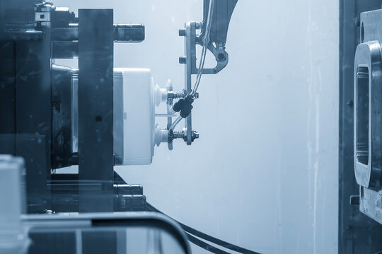 Automatic material handling of plastic parts from injection machine using robotic arm in blue tone lighting