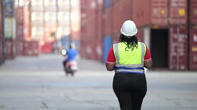 One female logistics worker uses a two way radio and hand signals to direct cargo operations at a shipping container yard. Concept of logistics, freight transport, communication, and supply chain.
