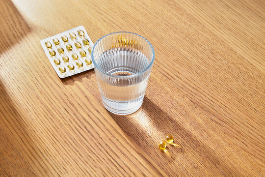 Vitamins and Glass of Water on Wooden Table