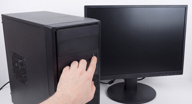 Close up of person finger pressing power button on front panel of black desktop personal computer tower standing beside black monitor