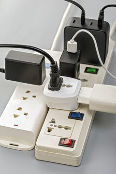Close-up of overloaded electrical power strips with multiple plugs, adapters, and USB chargers connected in a risky daisy chain arrangement, illustrating electrical hazard concept