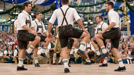Fototapeta premium Bavarian folk dance troupe performing synchronized steps in traditional lederhosen, oktoberfest stage show, alpine heritage