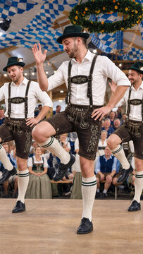 Schuhplattler folk dancers in lederhosen performing at Oktoberfest, traditional bavarian dance inside beer tent, cultural festival, tracht clothing, german folklore
