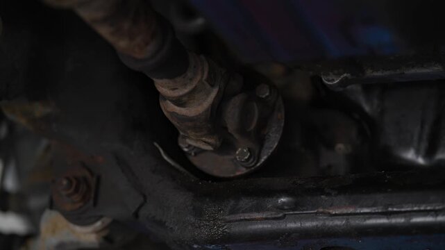 A close-up view of a car driveshaft universal joint connected to a flange underneath the vehicle chassis.