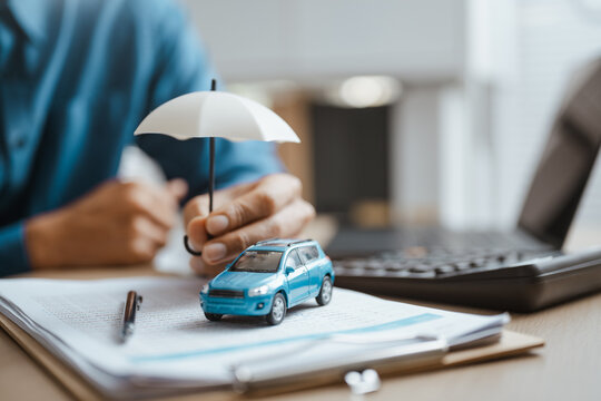 An insurance agent shields a car with an umbrella as insurance protection unites policy and vehicle coverage with finance, security, trust and care for an auto loan or dealership contract.