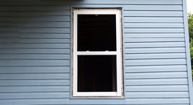 Close up view of energy efficient white vinyl window newly installed into light blue horizontal siding exterior wall