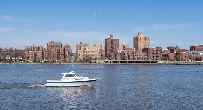 Sleek white motorboat sailing along a wide river waterway in front of an urban city waterfront and residential skyline