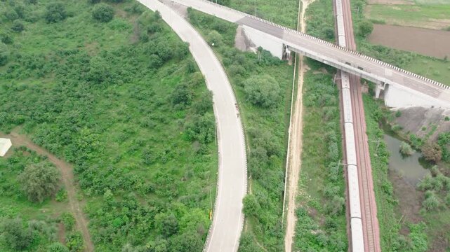 Aerial view of the Western Peripheral Expressway with a passing train on adjacent tracks surrounded by lush green vegetation in Gurugram, Haryana, India.