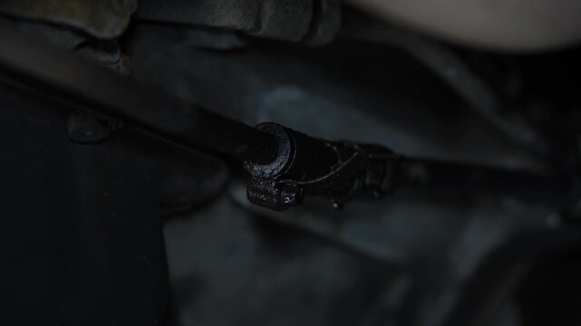 A dark, oily car steering shaft universal joint and rod assembly located underneath the engine bay.