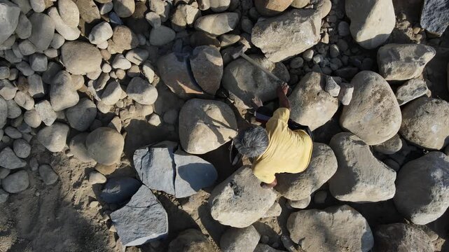 Aerial view of a worker using a hammer to break large stones in a quarry in Karanglewas, Central Java, Indonesia.