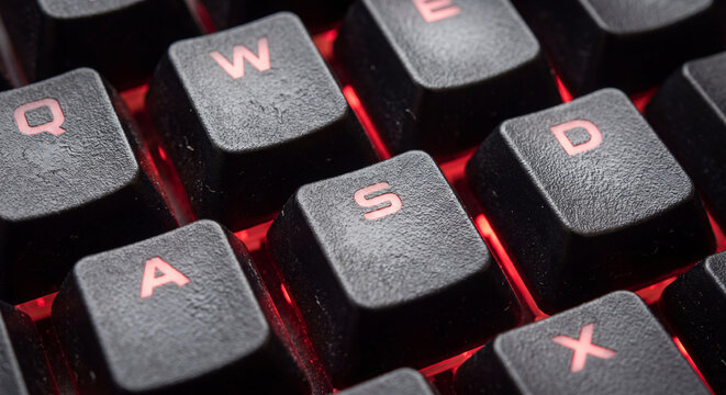 Close up macro view of mechanical computer keyboard keys with glowing red LED backlighting highlighting the WASD keys for gaming