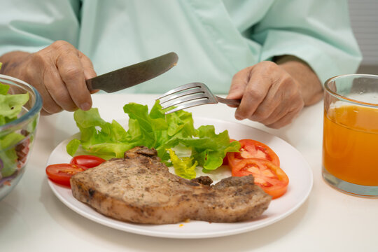 Asian elderly woman patient eating salmon stake and vegetable salad for healthy food in hospital.