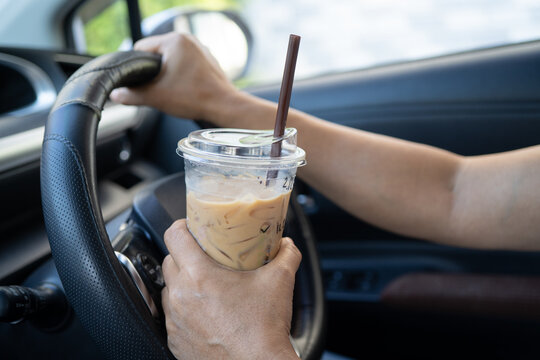 Asian lady holding ice coffee to eat in car, dangerous and risk an accident.